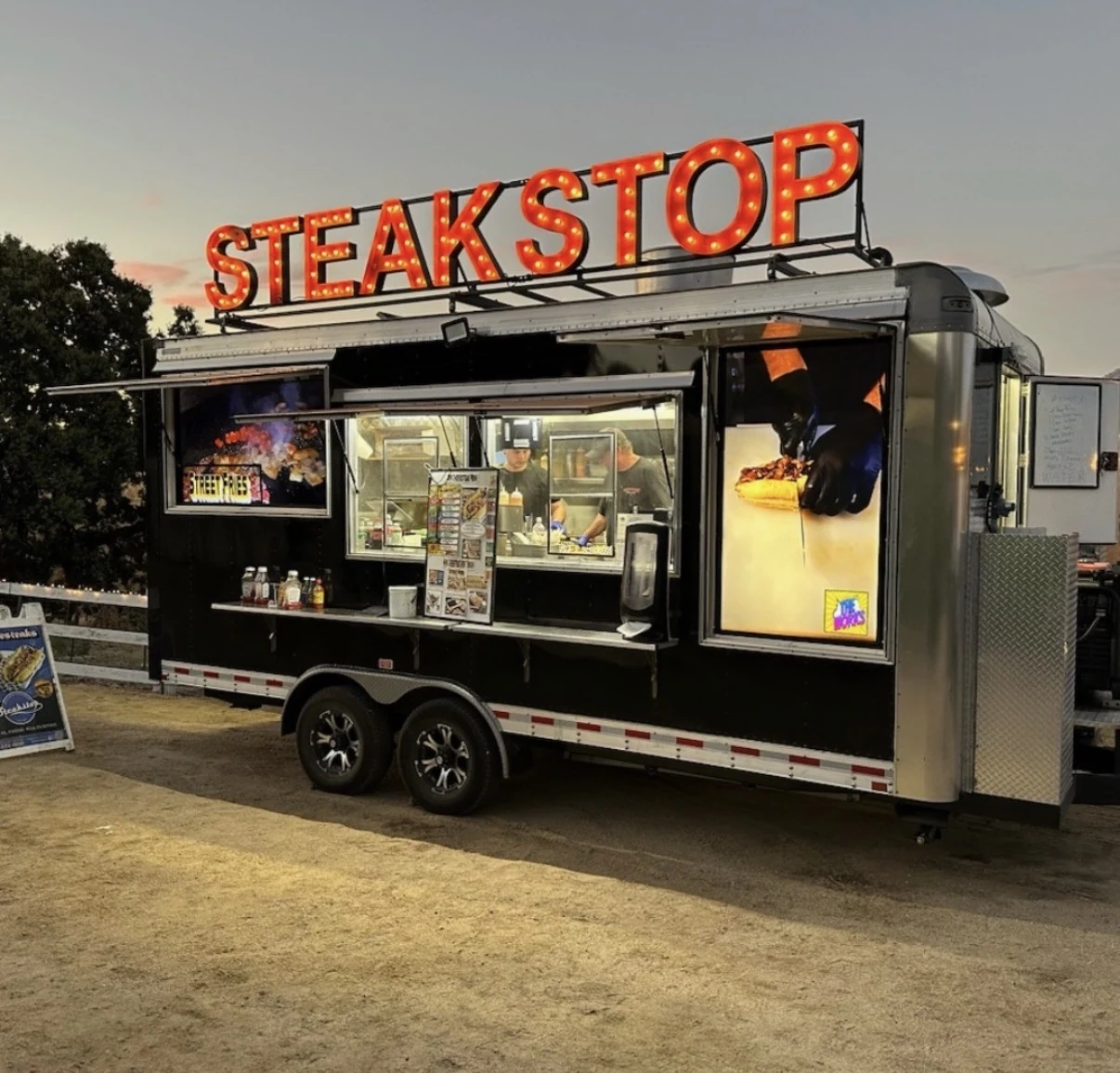 STEAKSTOP illuminated red letters installed above a black food trailer