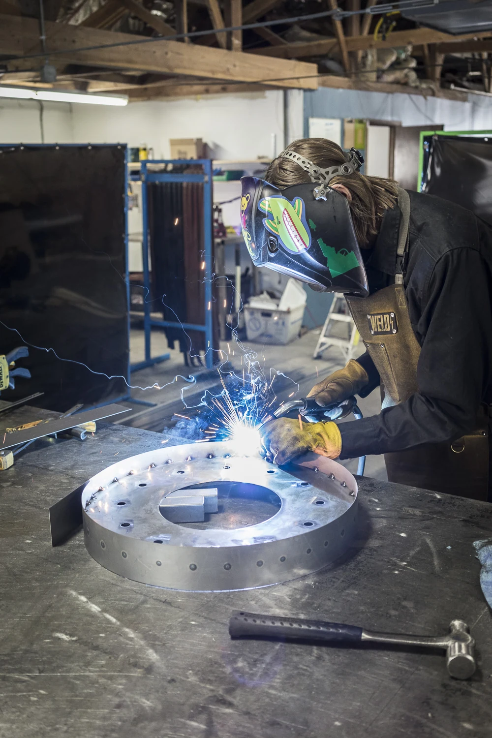 Fabrication crew member welding a round metal sign in the shop