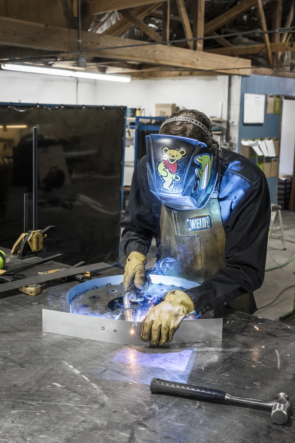Fabrication crew member welding a curved metal piece at a worktable