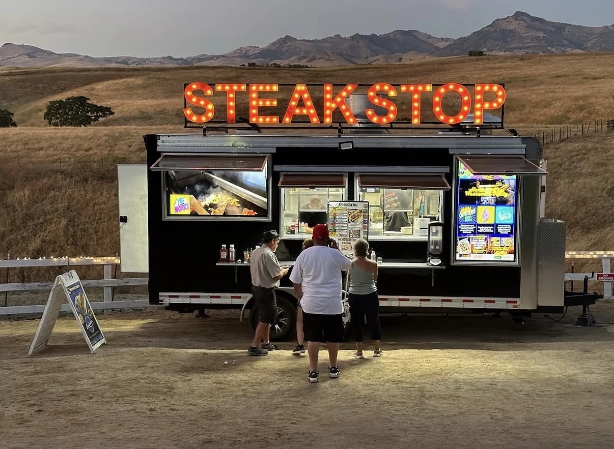 Straight-on view of illuminated STEAKSTOP letters above the food trailer